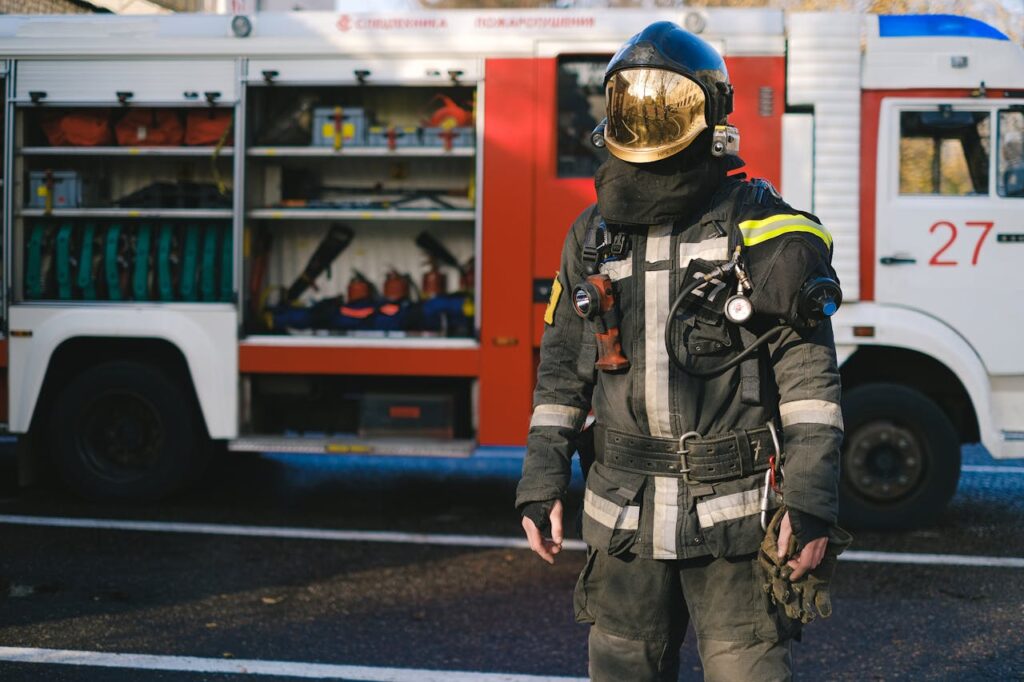 Firefighter in protective suit standing next to equipped fire truck ready for duty.