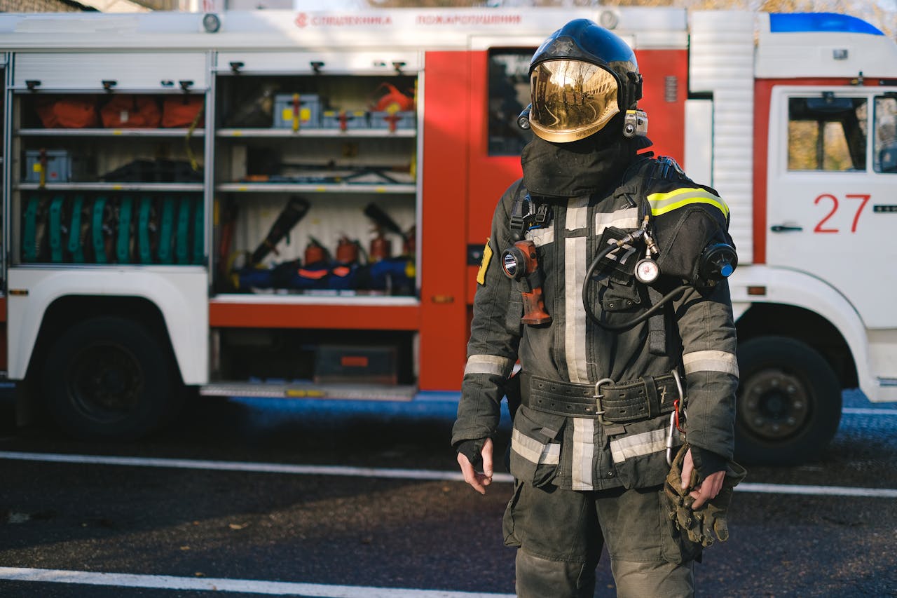 Firefighter in protective suit standing next to equipped fire truck ready for duty.
