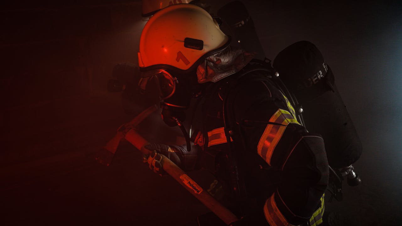 Firefighter in protective gear with helmet and axe in smoke-filled scene.